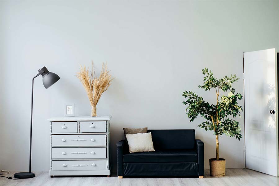 white-wooden-dresser-blue-leather-coach-small-area-lamp-cast-against-bare-white-wall-plant-decor | The Personal Helpers