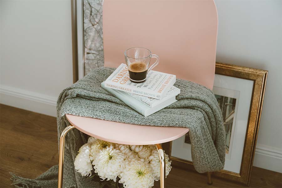 pink-chair-holding-grey-scarf-with-three-books-and-glass-on-top-against-the-wall