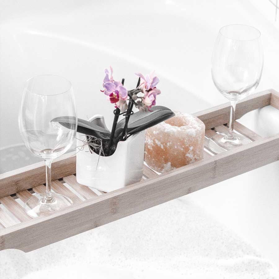 two-wine-glasses-with-plant-white-rectangular-pot-with-pink-petals-suspended-on-wood-bathtub-tray