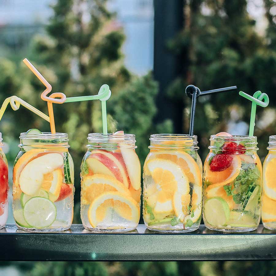 several-drinks-in-mason-jars-outdoors-summer-themed-arrangement-in-a-row