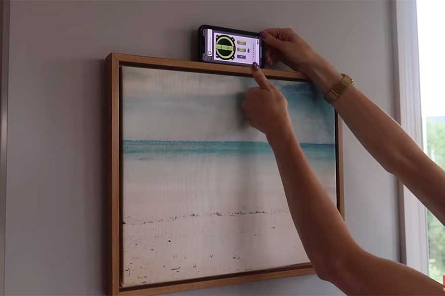 Woman using painters tape and phone app to correctly position and hang pictures