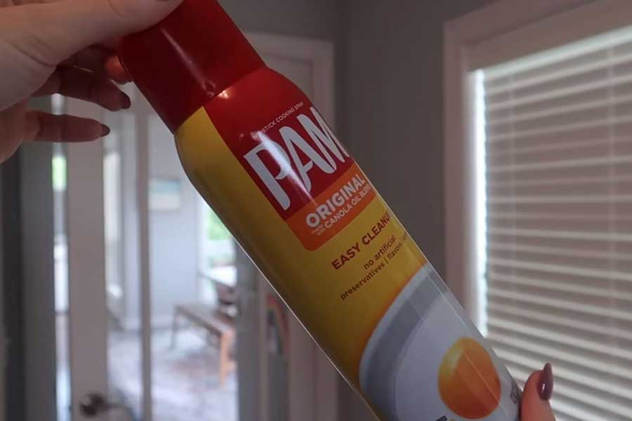 A person holding Pam cooking spray ready to lubricate a squeaky door hinge