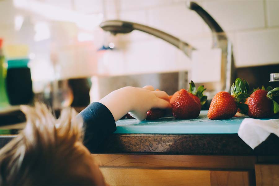 Child grabbing strawberries of an uncluttered countertop